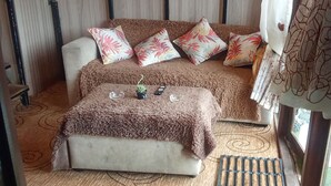 A cozy room with a sofa and ottoman, a small table with a plant, and a window with curtains. - The heaven wood cabin (Nuwaraeliya)