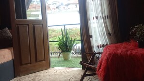 A room with a wooden door, a red furry chair, a green potted plant, and a view of a street through the window. - The heaven wood cabin (Nuwaraeliya)