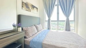 Een slaapkamer met een bed, een bureau, een stoel, een raam met gordijnen en uitzicht op de stad.