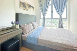 Un dormitorio con cama, escritorio, silla, ventana con cortinas y vista a la ciudad.