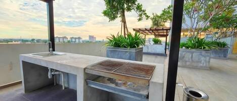 Un área de cocina al aire libre con pileta, parrilla y plantas en macetas.