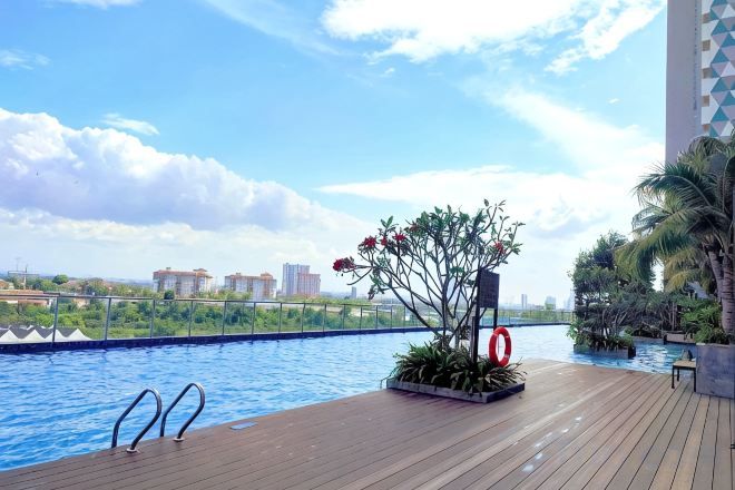 Un área de piscina en la azotea con cubierta de madera, escalera metálica y jardinera con flores.