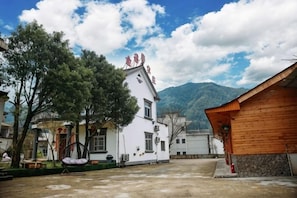 A courtyard with a white building, a wooden structure, and mountains in the background.