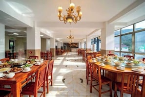 A spacious dining area with multiple tables and chairs, large windows, and a chandelier.