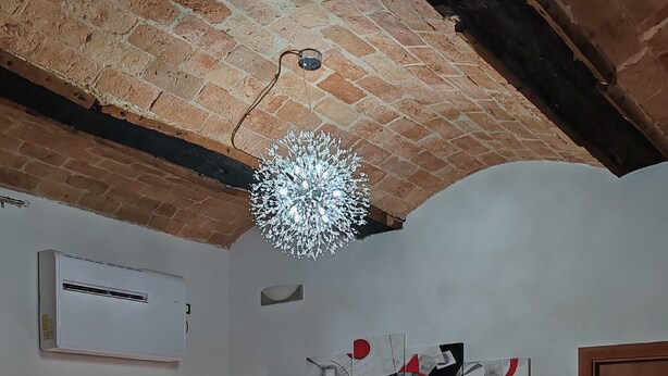 A bedroom with a bed, nightstands, a wall-mounted air conditioner, a ceiling light fixture, and a door. - Casa del Prof - Holiday apartment in the historic center (Asti)