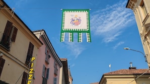A street view with a building labeled "PIZZERIA" and a banner with a coat of arms. - Casa del Prof - Holiday apartment in the historic center (Asti)