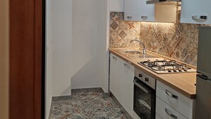 A compact kitchen with a gas stove, white cabinets, patterned backsplash, and a tiled floor. - Casa del Prof - Holiday apartment in the historic center (Asti)