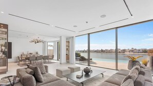 Ein modernes Wohnzimmer mit großem Fenster mit Blick auf ein Gewässer, einem Essbereich und einer Küche.