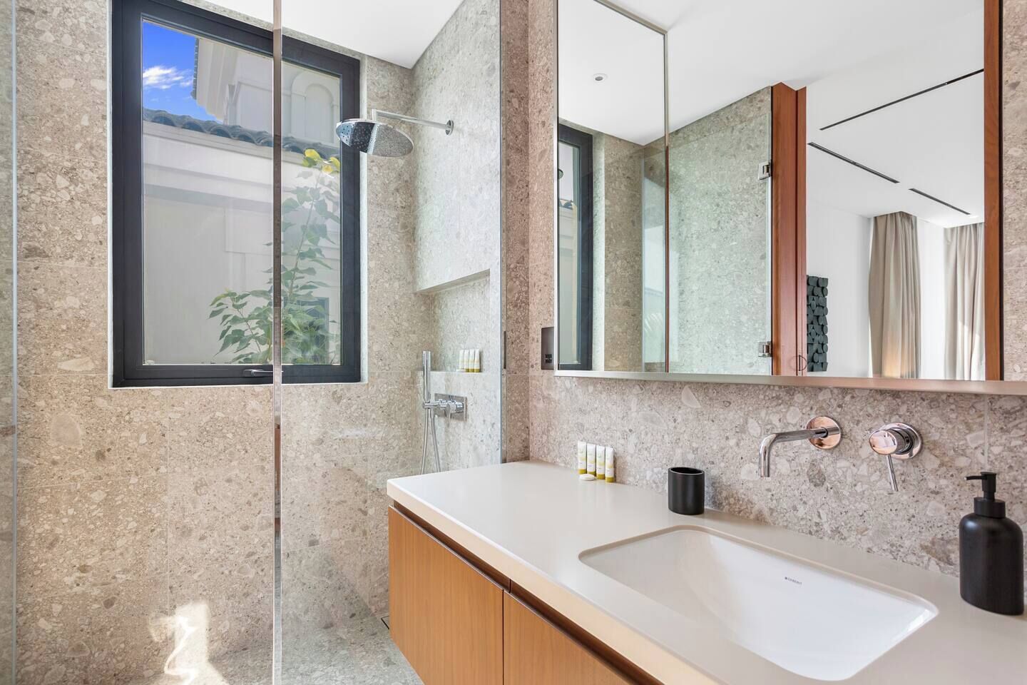 Een moderne badkamer met een grote spiegel, een douche en een wastafel met zeepdispenser.