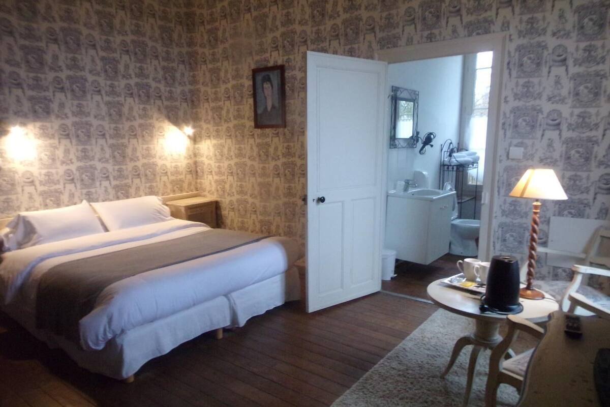 Ein Schlafzimmer mit Bett, Nachttisch, Schreibtisch mit Lampe und einem durchgegangenen Tür sichtbaren Badezimmer.