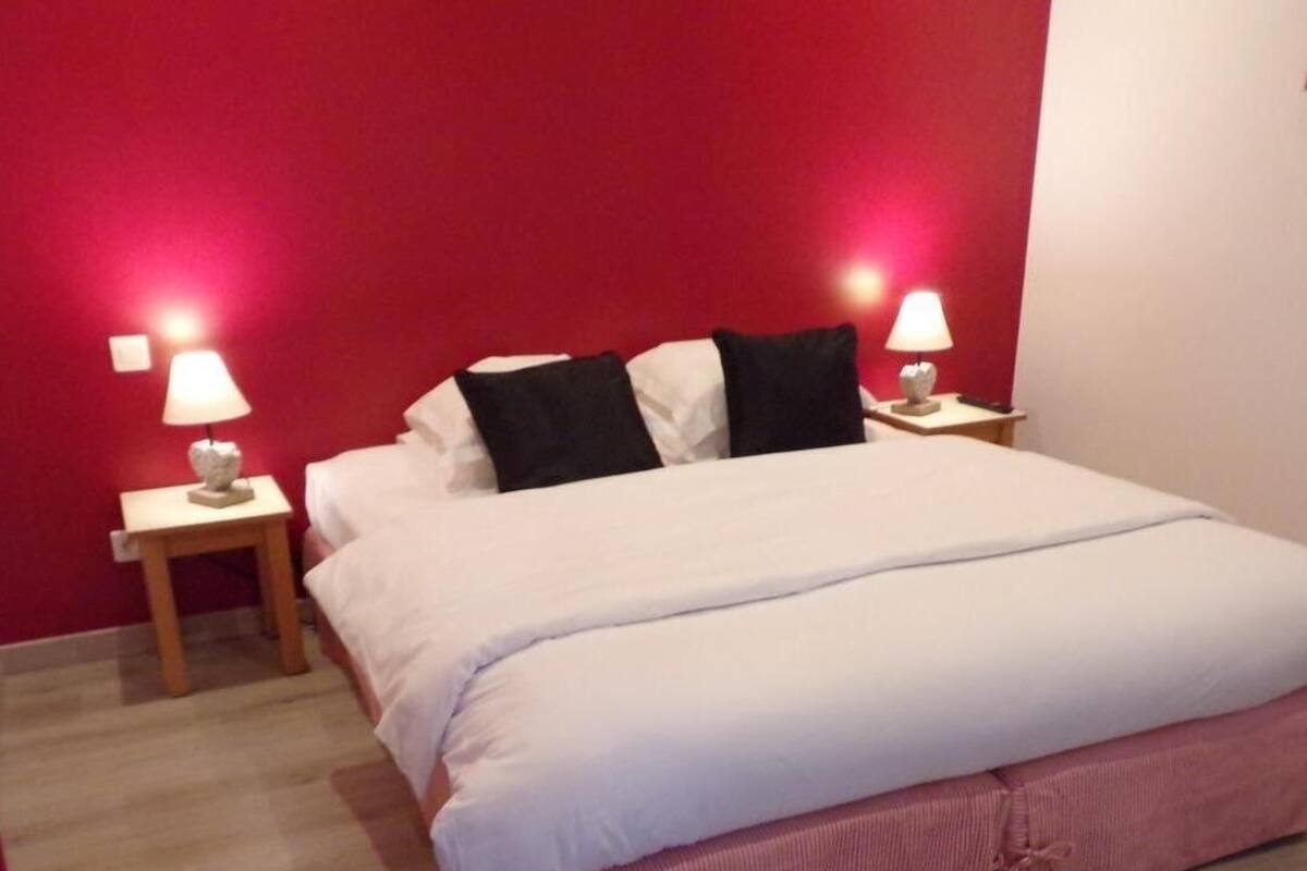 Ein ordentlich bezogenes Bett mit weißer und rosa Bettwäsche, zwei Nachttischlampen und einer roten Wand.