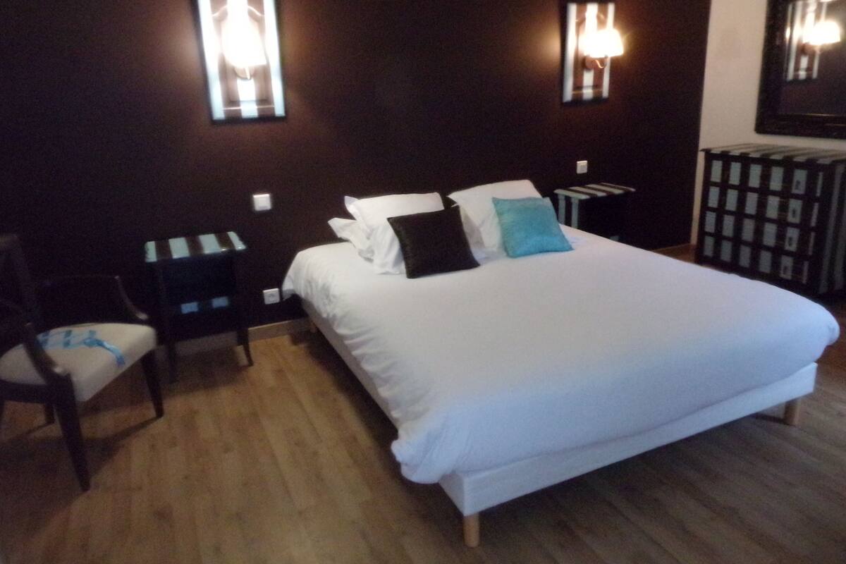 Ein Hotelzimmer mit einem großen Bett, zwei Nachttischen, einem Sessel und einem Spiegel an der Wand.