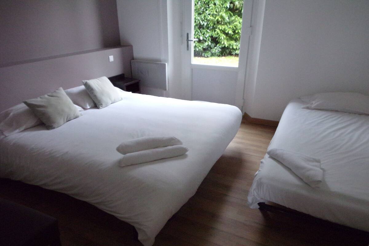 Ein Schlafzimmer mit zwei Betten, einem Nachttisch und einem Fenster mit Blick auf Grünflächen.