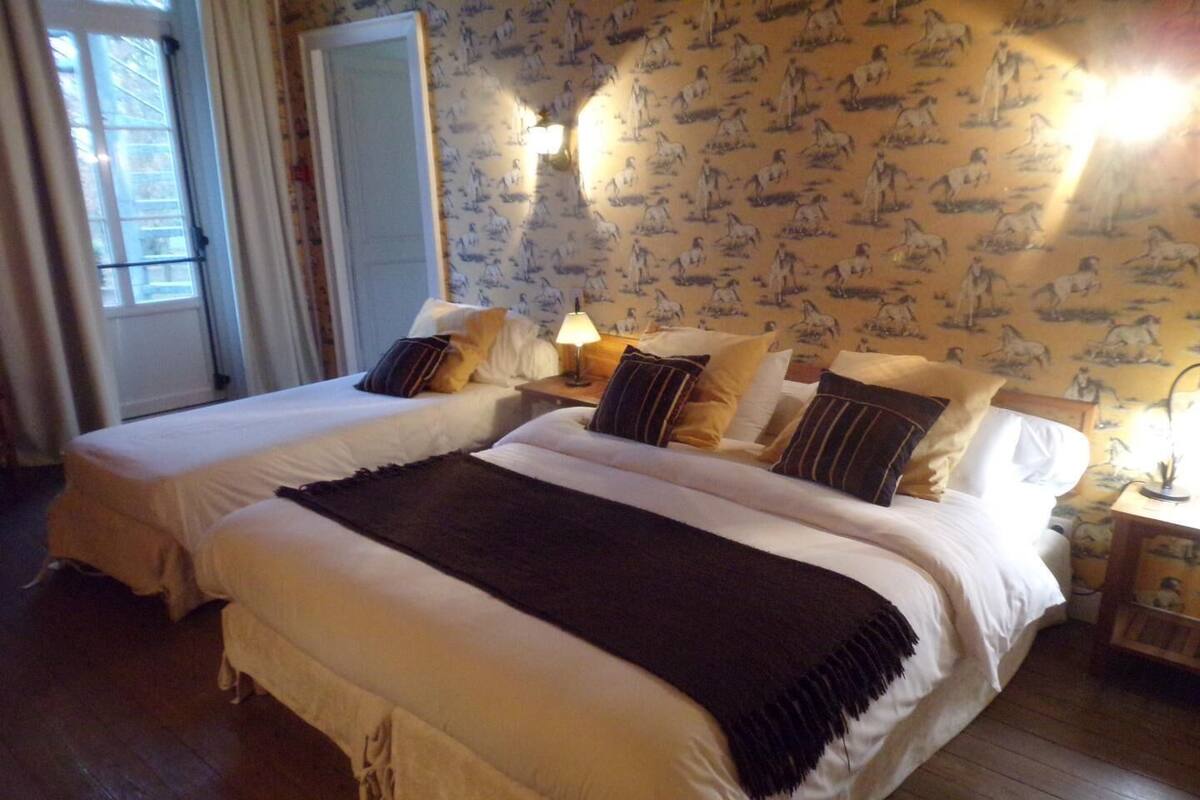 Ein Hotelzimmer mit zwei Betten, einer großen, dunkelgrauen Tagesdecke und einer Wand mit einem Pferdemotiv.