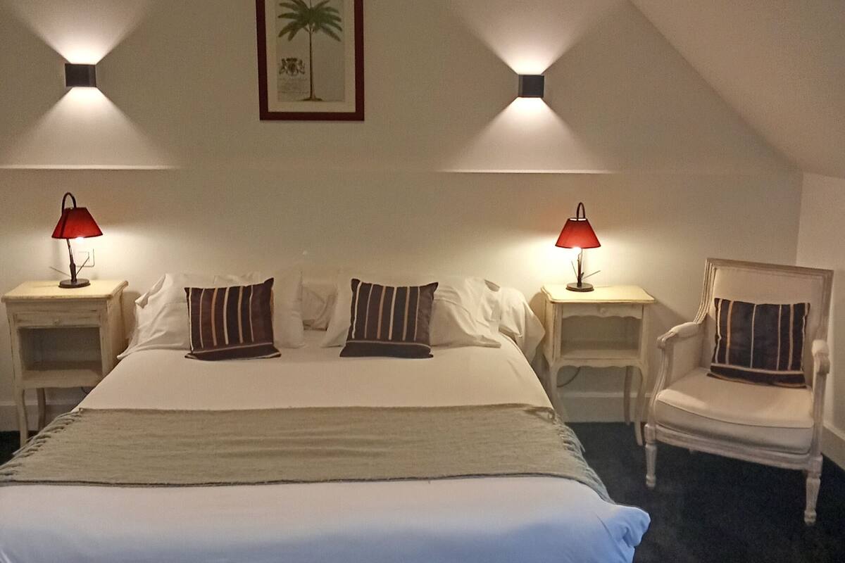 Ein Schlafzimmer mit einem großen Bett, zwei Nachttischen mit Lampen, einem Sessel und einem gerahmten Bild an der Wand.