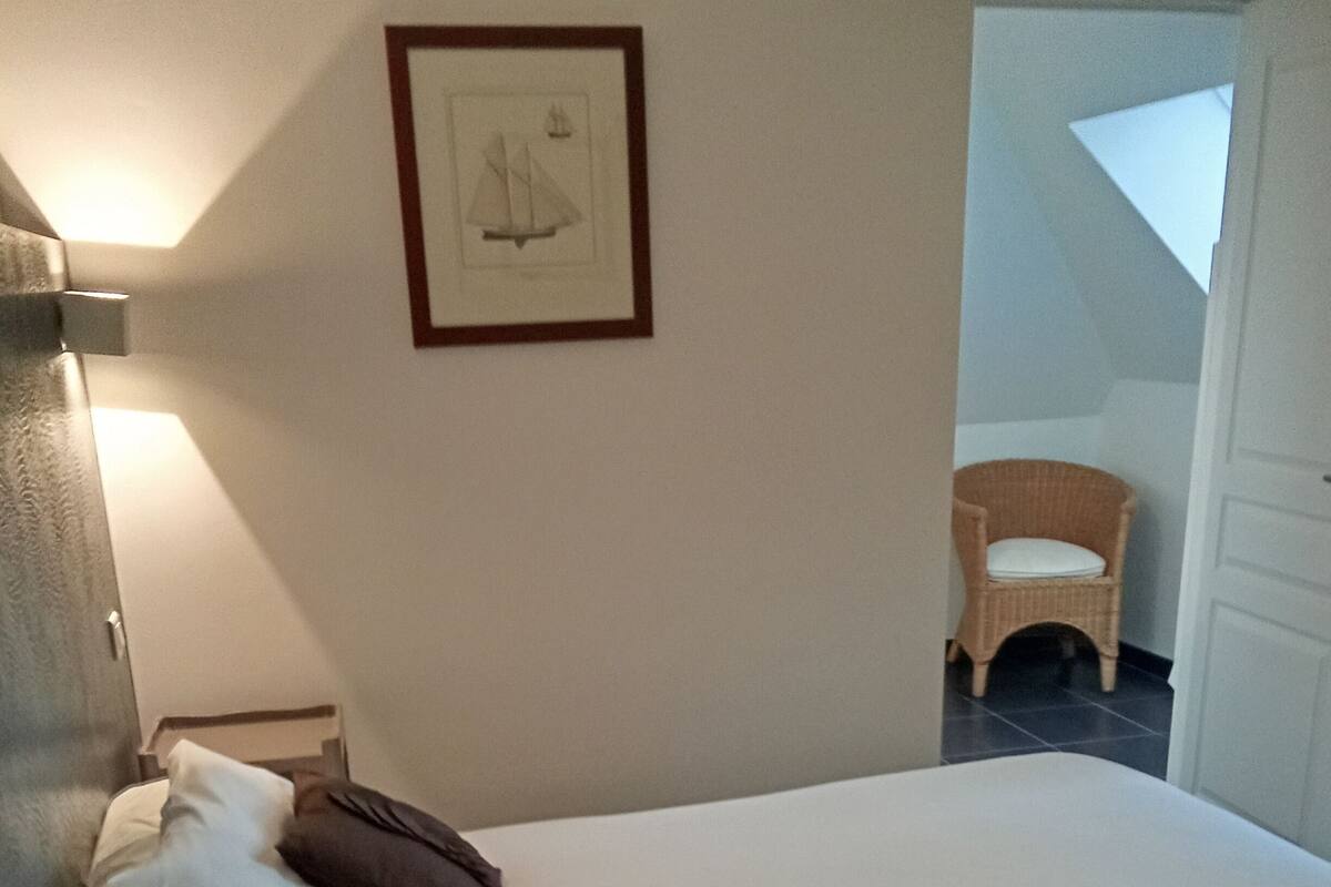 Ein ordentlich bezogenes Bett mit Kissen, ein gerahmtes Bild an der Wand und ein Sessel in der Ecke.