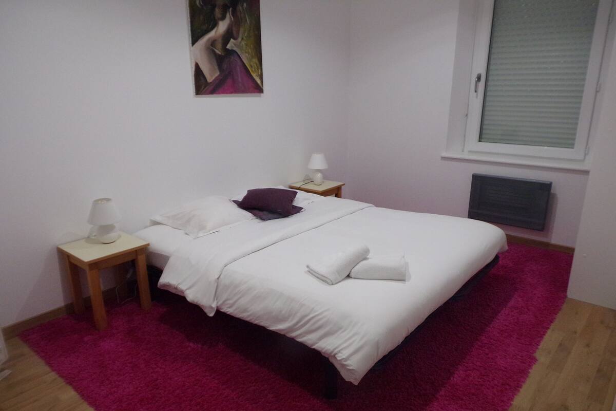 Ein Schlafzimmer mit einem Bett, zwei Nachttischen, einem Fenster und einem Bild an der Wand.