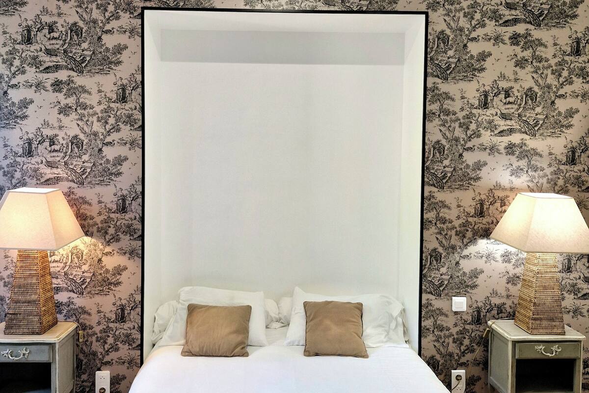 Ein Schlafzimmer mit einem großen Bett, zwei Nachttischen inklusive Lampen und blumigem Wandpapier.