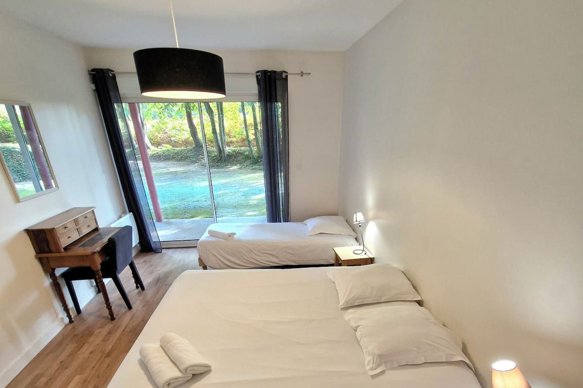 Ein modernes Schlafzimmer mit zwei Betten, einem Schreibtisch und Blick auf einen Garten.