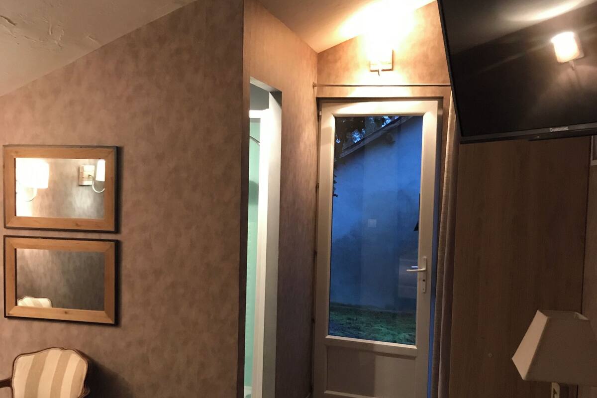 Ein Hotelzimmer mit Holzboden, einem an der Wand montierten Fernseher, einer Tür zu einem Balkon und zwei gerahmten Spiegeln an der Wand.