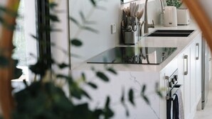 Une cuisine moderne dotée d’une hotte en acier inoxydable, d’un évier avec un robinet et d’un plan de travail agrémenté d’une plante et d’ustensiles de cuisine.