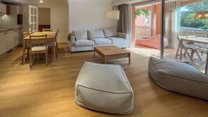 A modern living room with a sofa, coffee table, and ottoman, a dining area with chairs, and a kitchen in the background. - Cosy T3 5 minutes from beaches and town center (Sainte-Maxime)
