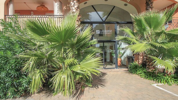A hotel entrance with a palm tree-lined pathway, an arched doorway, and a sign indicating availability. - Cosy T3 5 minutes from beaches and town center (Sainte-Maxime)