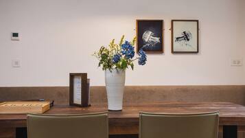 Une table en bois sur laquelle est posé un vase blanc rempli de fleurs, une œuvre d’art encadrée au mur et une boîte en bois portant le mot « LICHEN ».