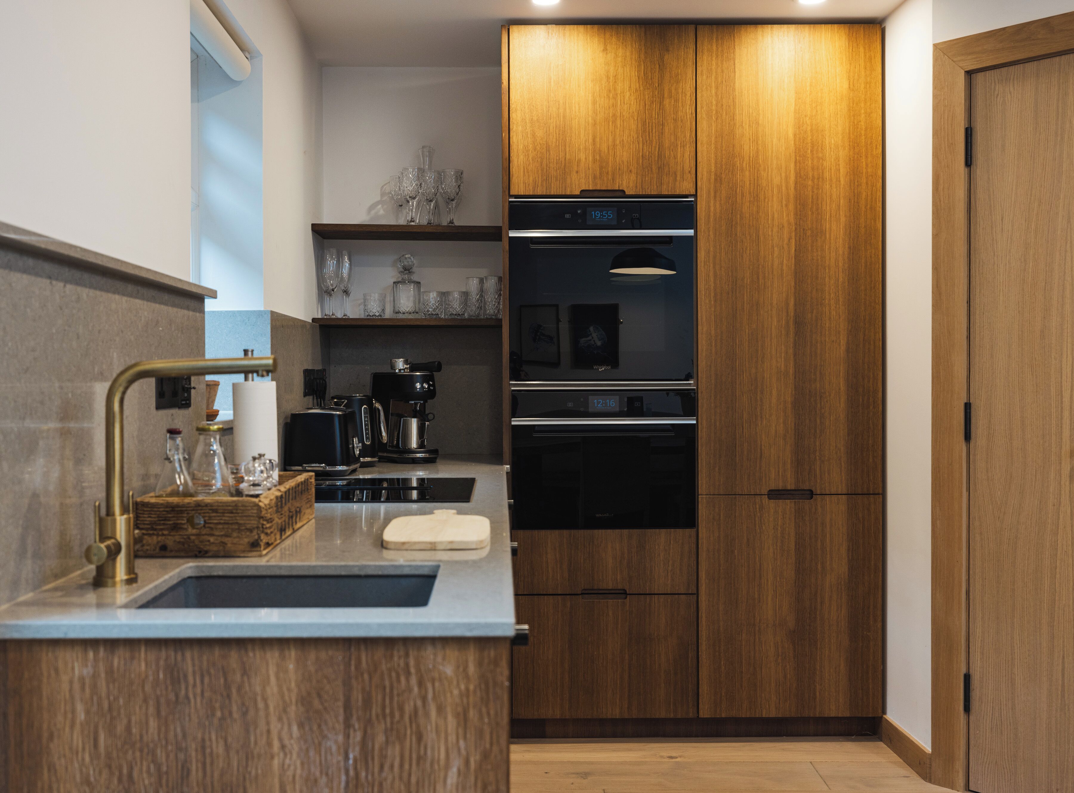 A modern kitchen with wooden cabinets, a built-in oven, a coffee maker, and a sink.