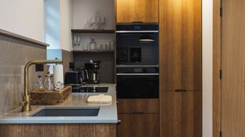 A modern kitchen with wooden cabinets, a built-in oven, a coffee maker, and a sink.