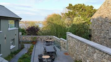 Eine Terrasse mit Sitzgelegenheiten, eine Steinmauer und Blick auf ein Gewässer und Bäume.