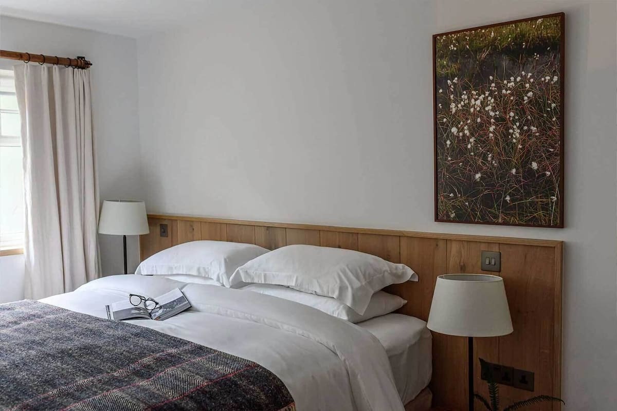 A hotel room with a bed, two bedside lamps, a painting on the wall, and a window with curtains.