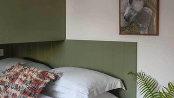 Ein Schlafzimmer mit einem Bett, Kissen, einem Nachttisch mit einem Buch und einer Pflanze, einer Wandlampe und einem Bilderrahmen mit einem Pferd.