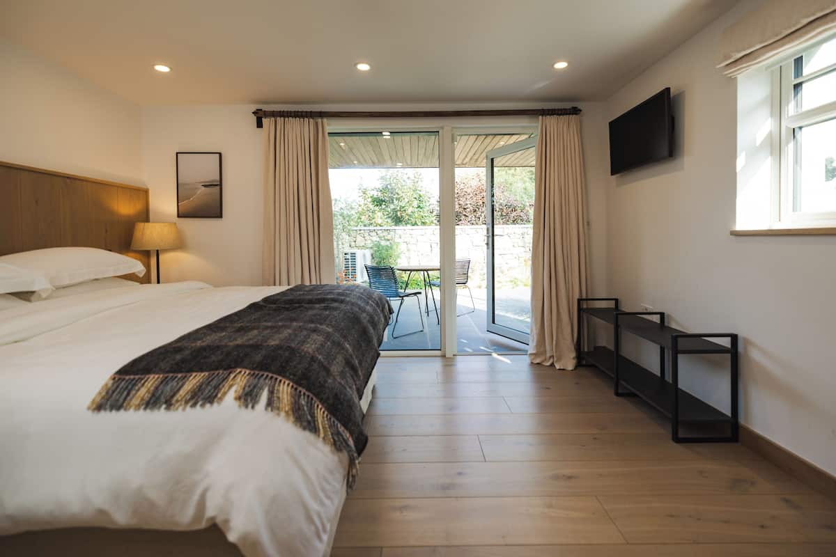A bedroom with a bed, a TV, a window, and a view of the outdoors.