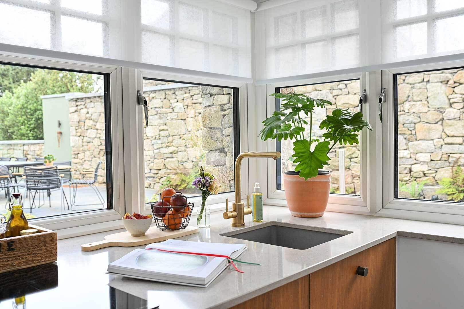 A kitchen with a stone wall view, a sink, a potted plant, and a bowl of fruit.