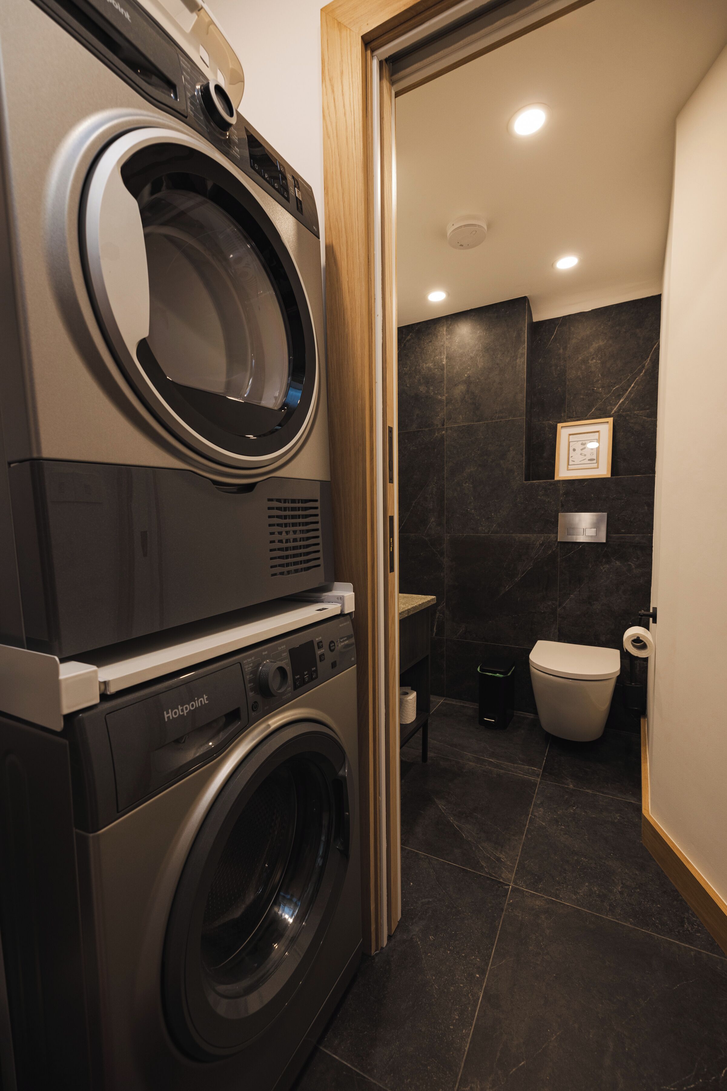 A compact laundry area with a front-loading washing machine and dryer, a toilet, and a shower.