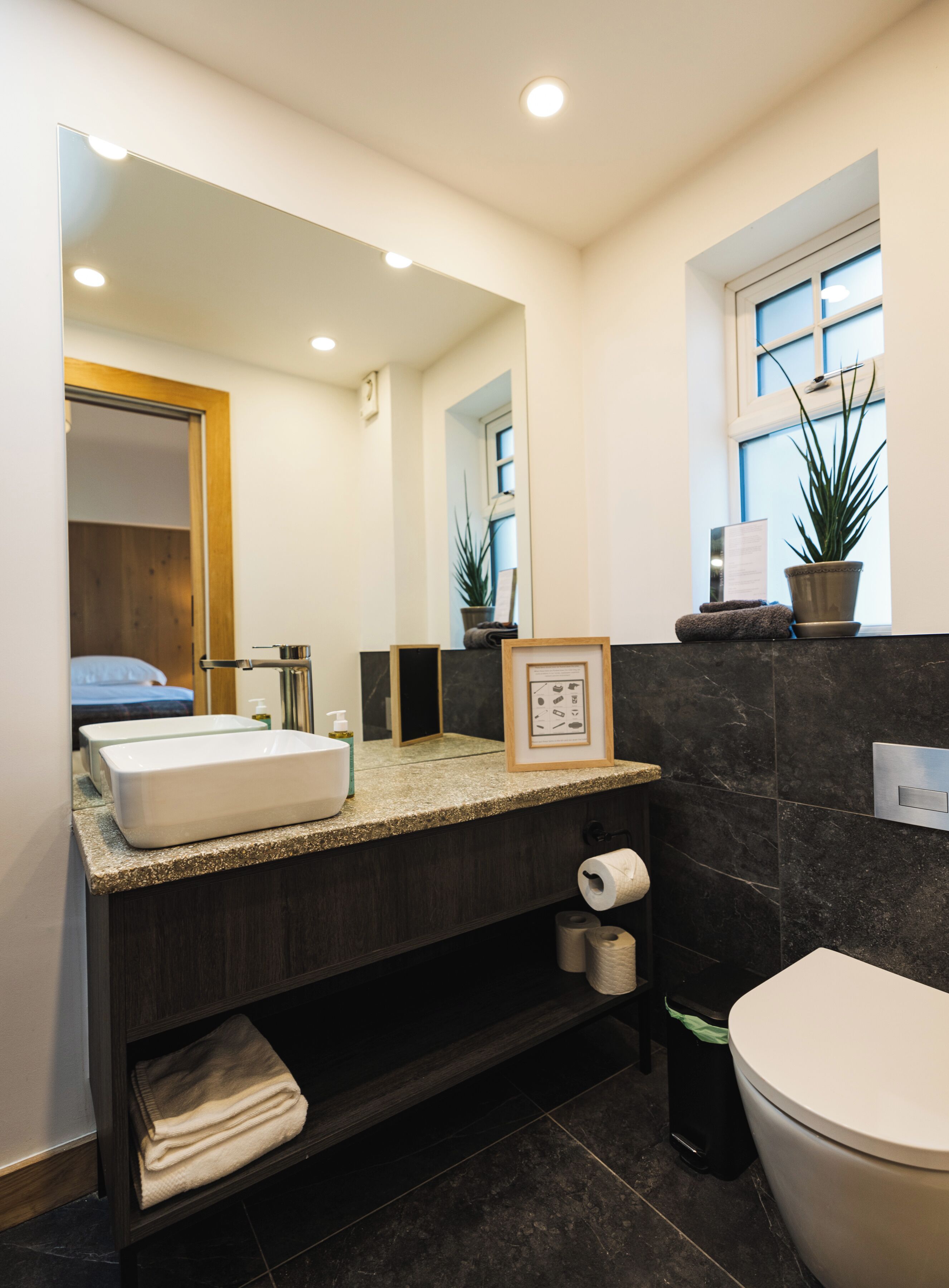 Un bagno moderno con uno specchio grande, un lavandino, un water e una finestra.