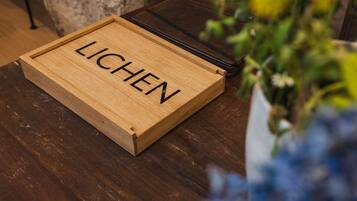 A wooden box with the word 'LICHEN' on it, placed on a wooden surface next to a black leather item.