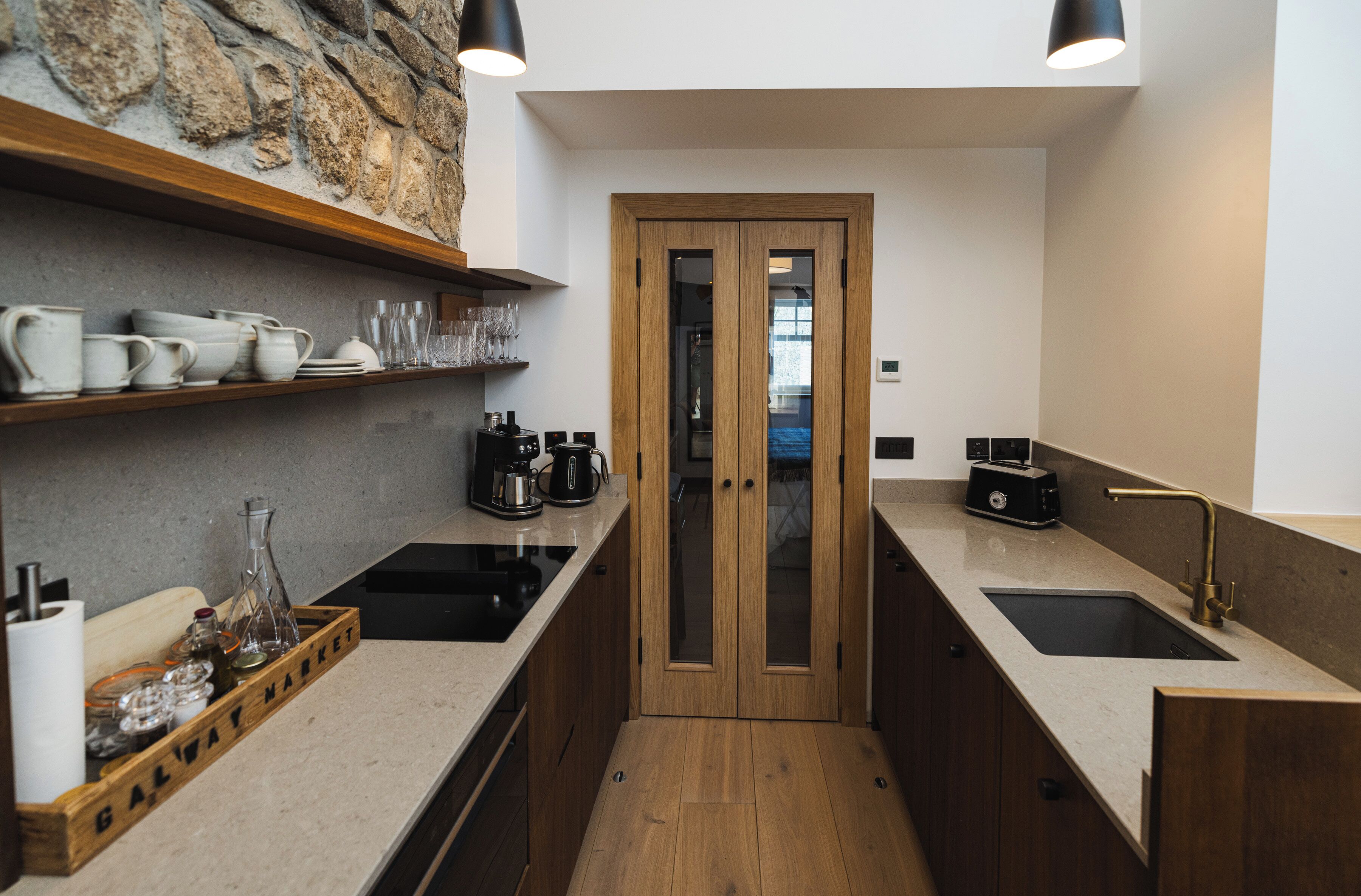 A modern kitchen with two sinks, wooden cabinets, and a stone accent wall.