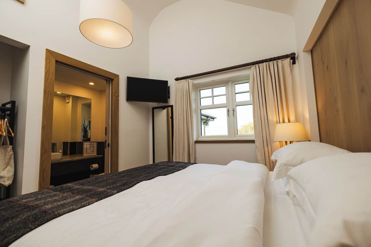 A hotel room with a bed, a television, a window with curtains, and a lamp.