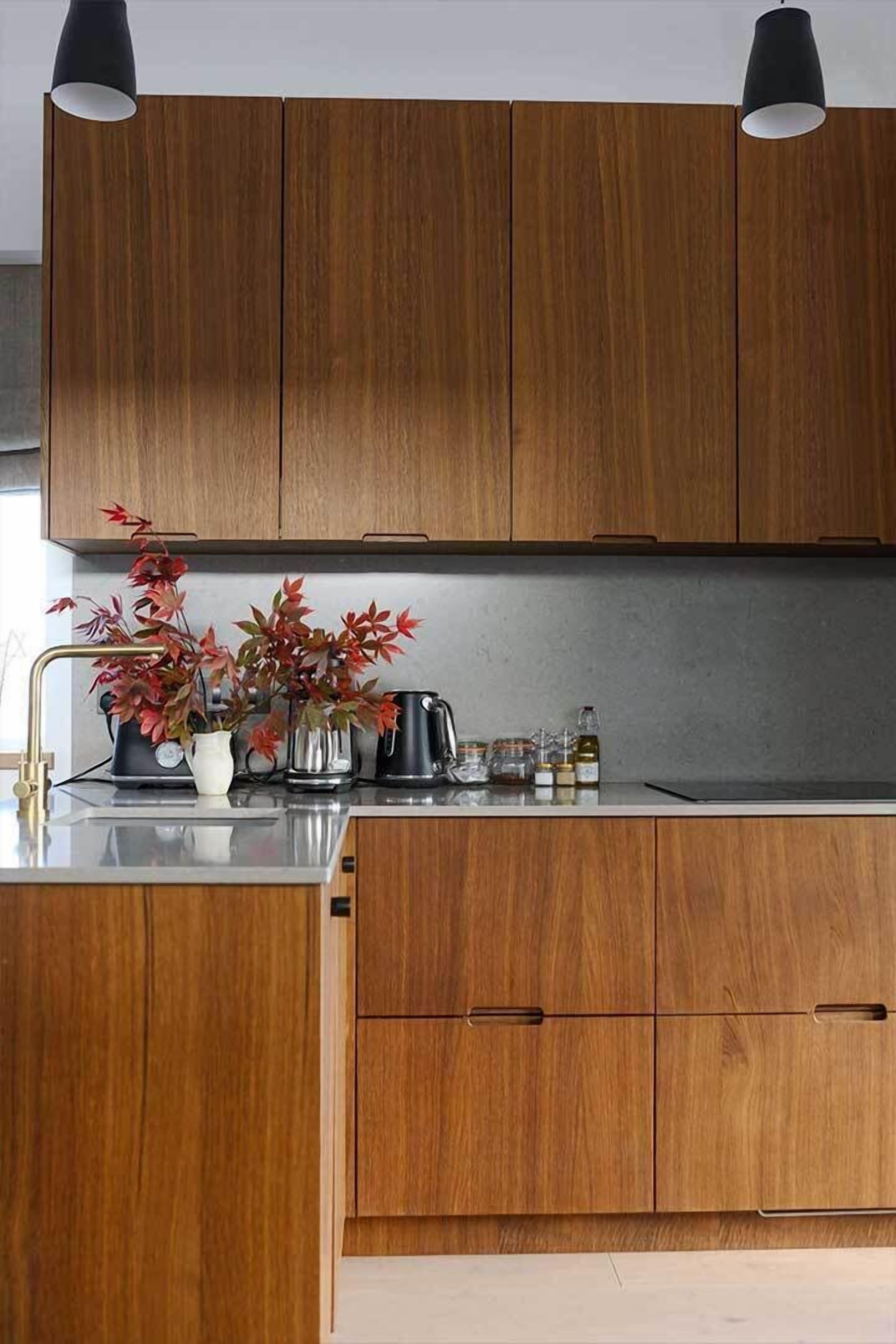 A kitchen with wooden cabinets, a countertop, a sink, a kettle, a clock, and a vase with red leaves.