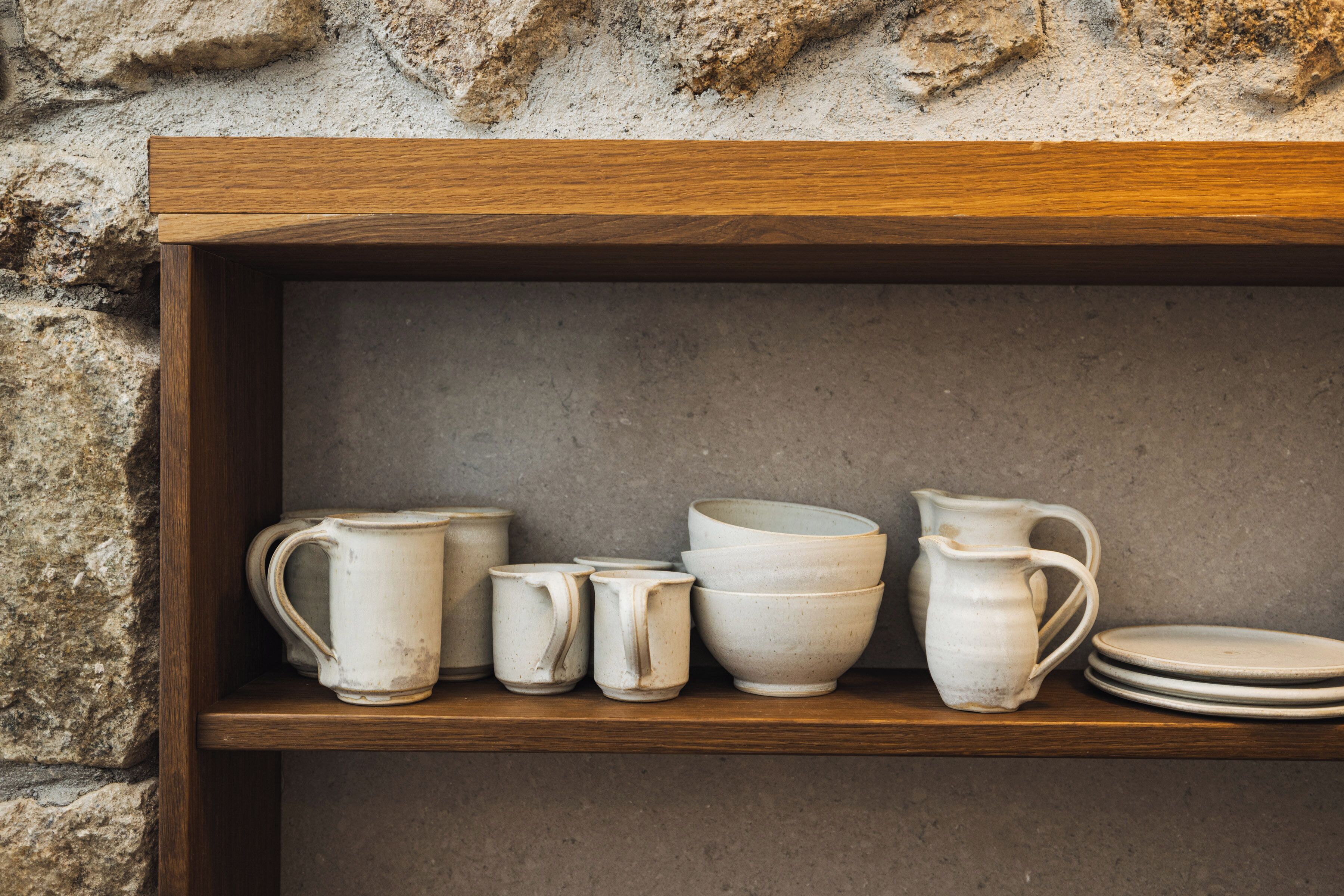A shelf with ceramic mugs, bowls, and a pitcher.