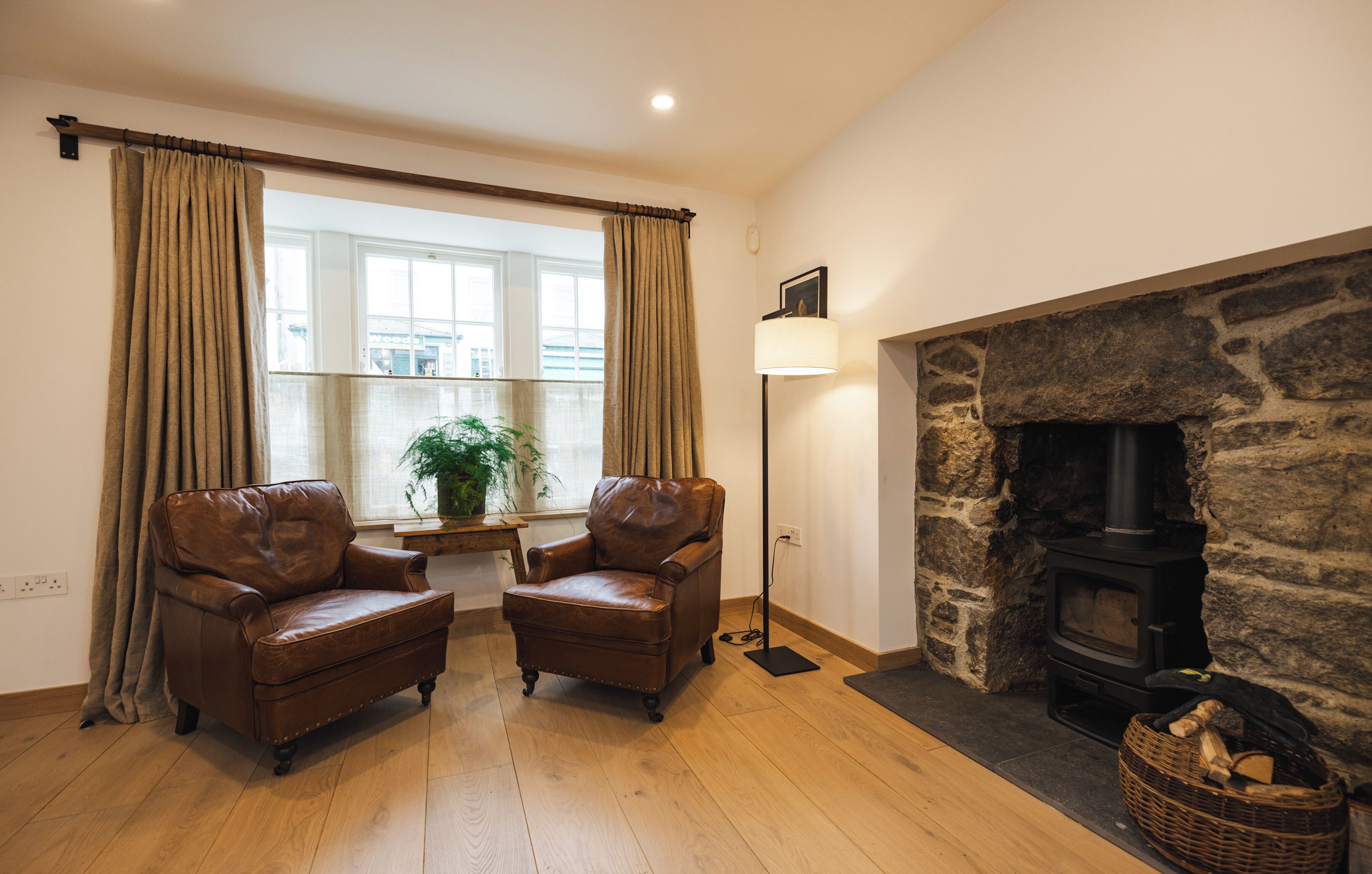 A room with a stone fireplace, two leather armchairs, a floor lamp, and a window with curtains.