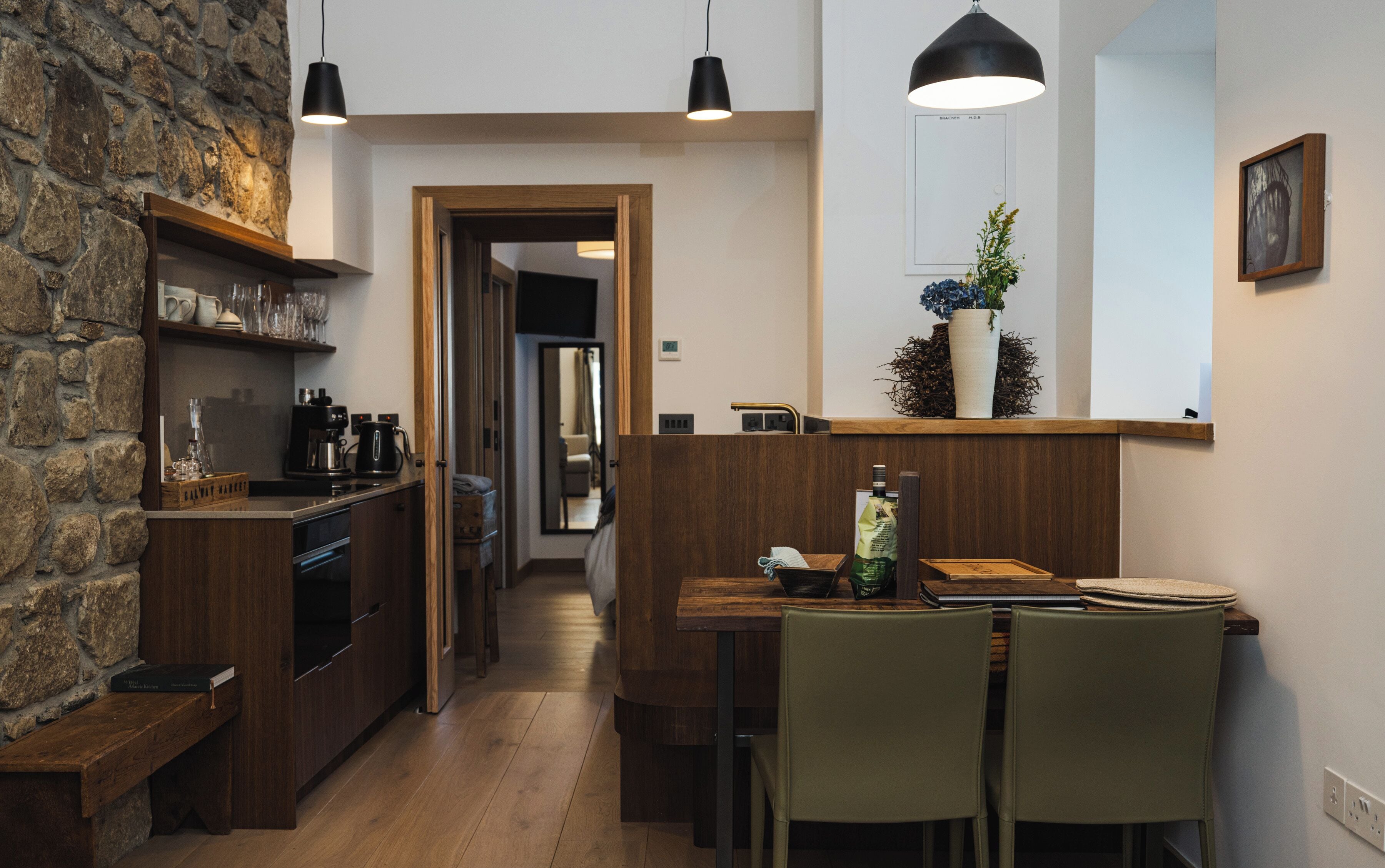 Una cocina moderna con armarios de madera, una zona de comedor con mesa y sillas, y una pared de piedra.