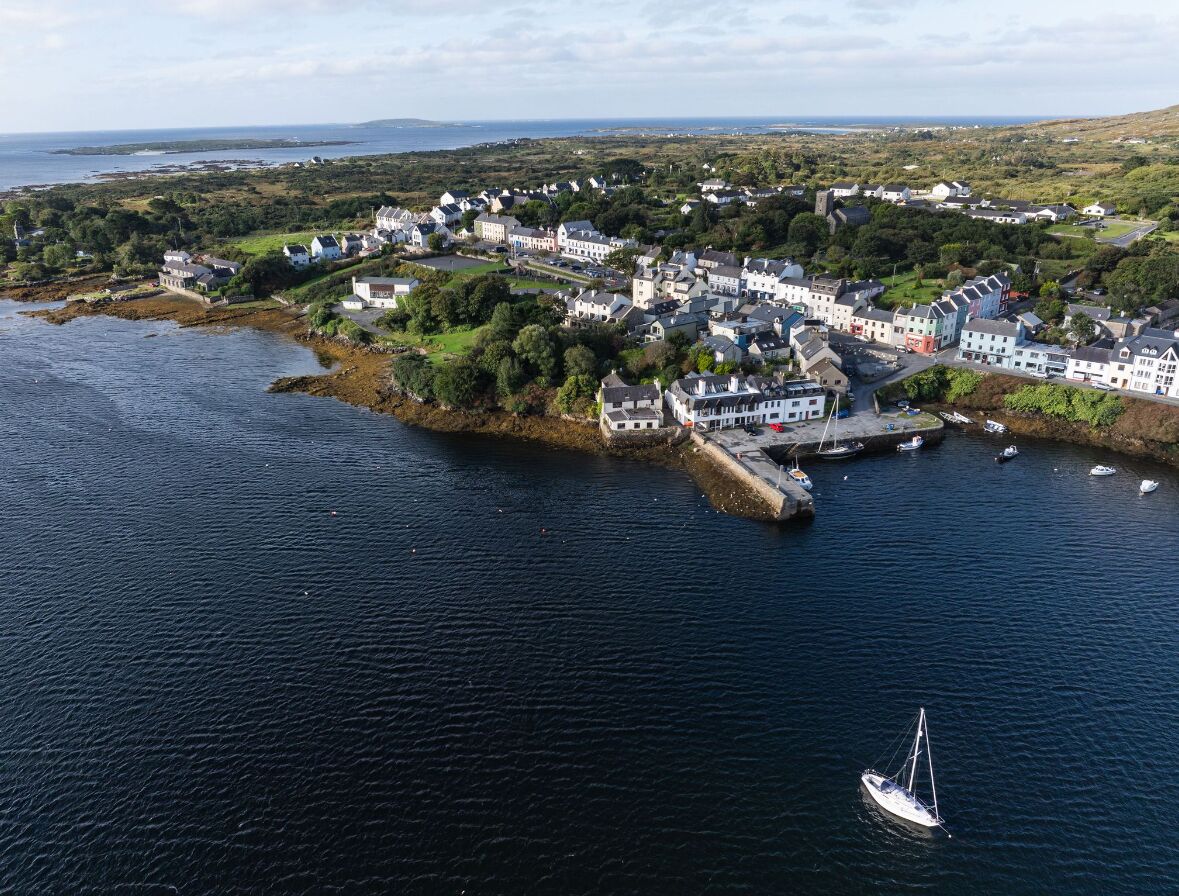 An aerial view of a coastal town with houses along the shoreline, a pier, and boats in the water.