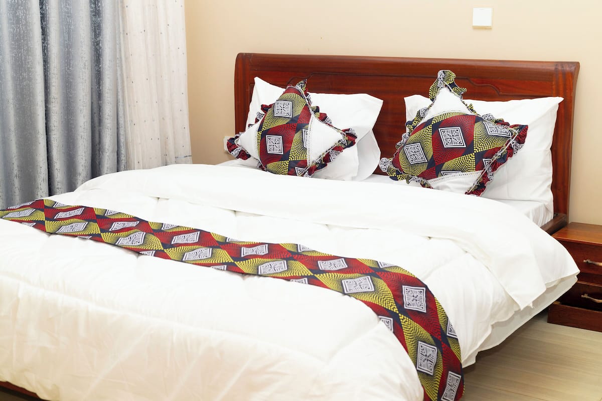 A neatly made bed with white linens and a colorful blanket, a wooden headboard, and a nightstand with a lamp.