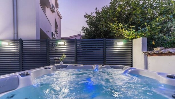 Ein Whirlpool mit Wasserfall, umgeben von einem Metallzaun und einem Gebäude im Hintergrund.