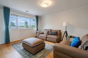 A living room with a sofa set, a standing lamp, and a window with curtains. - Spacious 4B House in PointCook (Point Cook)