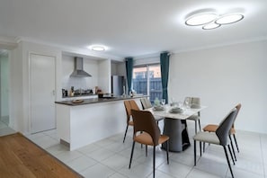 A modern kitchen with a dining area, featuring a central island, chairs, and a table set for dining. - Spacious 4B House in PointCook (Point Cook)