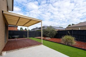 A backyard with a covered patio, a brick patio, a lawn, and a wooden fence. - Spacious 4B House in PointCook (Point Cook)